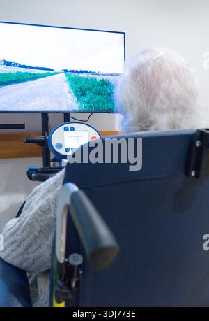 Elderly person exercising on a specialized rehabilitation machine using a screen for virtual therapy Stock Photo