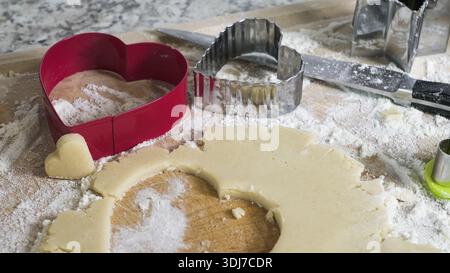 Heart cutters on a wooden board with dough and flour, preparing cookies Stock Photo