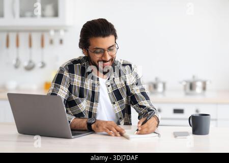 Positive arab guy looking for job online, kitchen interior Stock Photo
