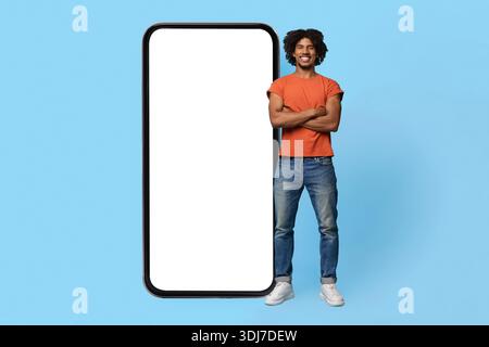 Confident black guy posing by big smartphone with empty screen Stock Photo