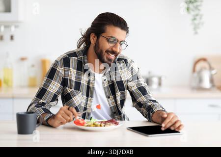 Happy indian guy having lunch and using digital tablet Stock Photo