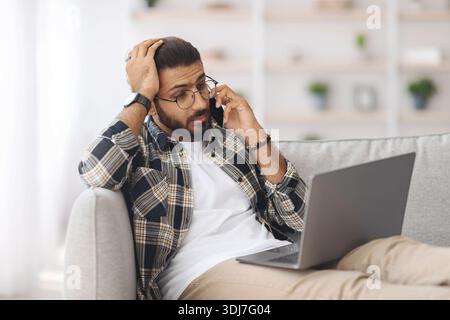 Stressful indian guy with laptop having phone conversation Stock Photo