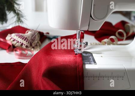 Sewing machine in action, with red fabric under the presser foot. Creative DIY Christmas-themed sewing project. Christmas and holiday season. Close-up. Stock Photo