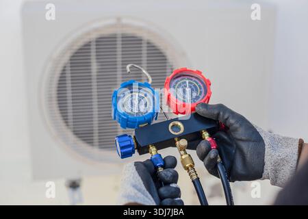 Air conditioning, HVAC service technician using gauges to check refrigerant and add refrigerant. Stock Photo