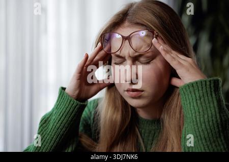 Frustrated young woman in glasses touching temples, suffering from headache or stress, eyes closed. Stock Photo