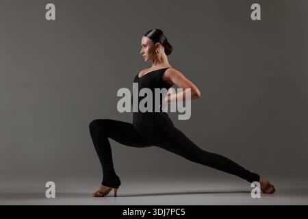 Confident female dancer in black bodysuit holding dramatic lunge pose, showcasing balance, strength, and expression. Stock Photo