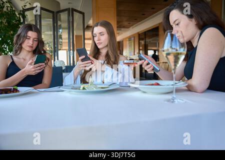 Three young woman using mobile phones sitting in the restaurant Stock Photo