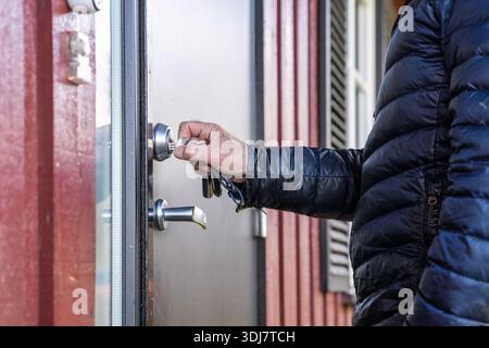 Individual in a black puffer jacket is using a key to unlock a door, highlighting the action of entering a space, with a focus on security and accessi Stock Photo