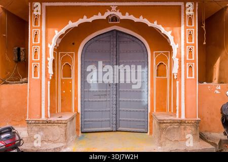 Jaipur, India - March 15, 2022: Ornate arched doorway with a large grey metal door set in an orange wall with white decorative trim and architectural details in the old city. Stock Photo