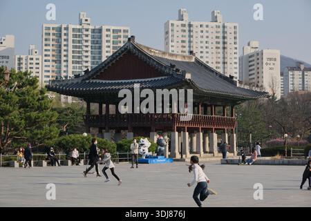 Seongnam, South Korea: Children playing on open square near traditional pavilion at Bundang Central Park with modern apartment buildings behind Stock Photo