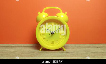 Modern yellow alarm clock on wooden surface with a bright orange wall backdrop Stock Photo
