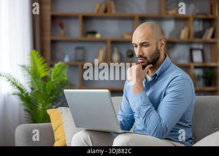 Young man concentrating on laptop, making decisions, or solving problems, capturing the essence of remote work and digital innovation in a contemporary home setting Stock Photo