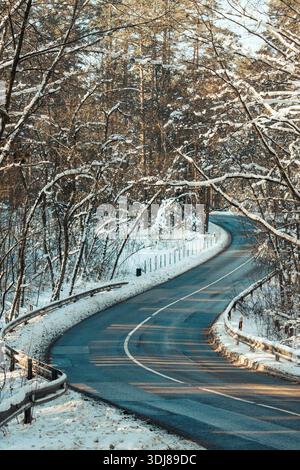 Slippery icy road through the forest with trees and snow on both sides Stock Photo