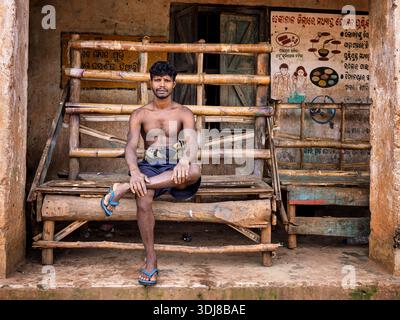 A man restring on a bench in a village in Odisha, India Stock Photo