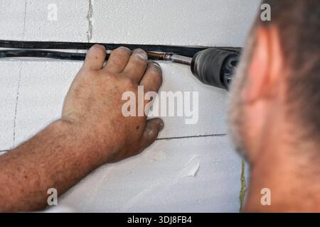 Electrician securing cables in groove or chase on a wall in newly built house, using power drill and screws - closeup detail Stock Photo