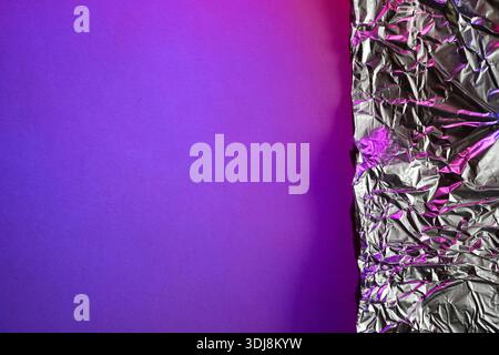 Crumpled metallic foil on vibrant purple background illuminated by neon pink light Stock Photo