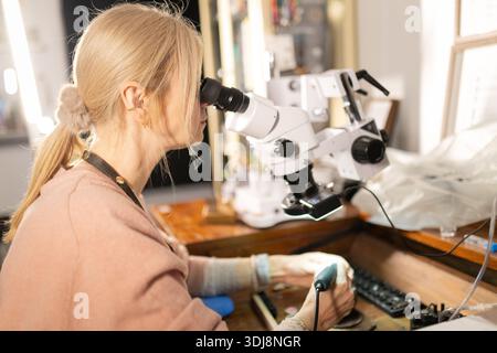 Woman jeweler examining intricate details using a microscope Stock Photo