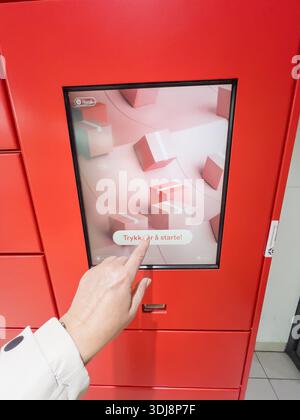 Porsgrunn, Norway - October 20, 2025: Hand pressing touchscreen on red Instabox locker system, illustrating user engagement with digital interface for Stock Photo