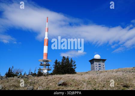 A tall broadcast tower rises above a rocky mountain landscape under bright blue skies and dynamic clouds. Stock Photo