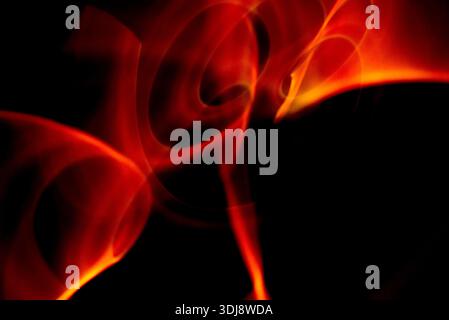 Intense red fire like energy waves forming abstract motion with glowing highlights on dark background. Stock Photo