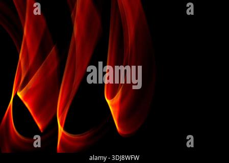 Flowing flame shaped waves creating abstract fiery motion with glowing orange red tones on dark background. Stock Photo