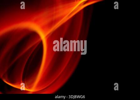 Smooth flowing orange fire shapes creating abstract energy movement on deep black background. Stock Photo