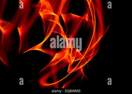 Chaotic fire smoke motion creating expressive abstract glowing shapes on deep black background. Stock Photo