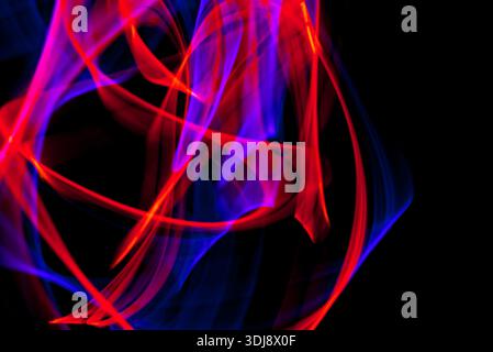 Intertwined red blue and green energy lights forming vivid abstract motion on black background. Stock Photo
