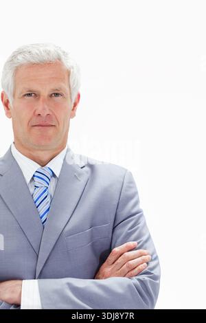 Senior male posing with arms crossed wearing light gray suit and striped tie in studio. Executive, headshot, corporate, leadership, professionalism, m Stock Photo