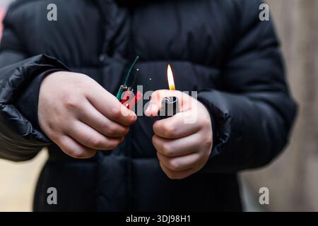 Boy lighting up several firecrackers in his hand using lighter. Kid getting ready for celebration with fireworks or pyrotechnic products . Boy holding Stock Photo