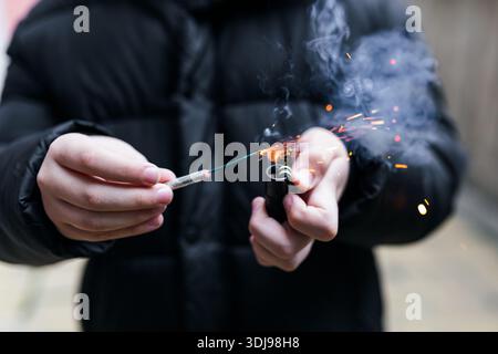 The firecracker in a hand. Boy holding a burning petard in his hand. Kid with a pyrotechnics that burns with sparks and smoke outdoors. Firecracker an Stock Photo