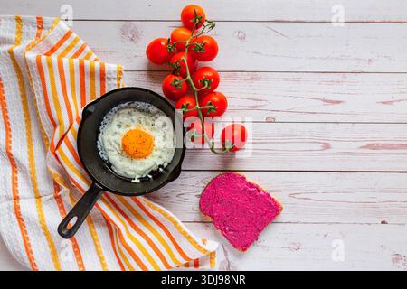 Breakfast time, Fried Egg in a cast iron pan with salad bowl , beetroot spread and fresh cherry tomatoes on wooden table Stock Photo