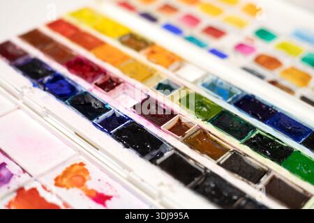 Watercolor pans in white plastic box for painting. Opened paint set for professional watercolor painter on white background. Used paint collection clo Stock Photo