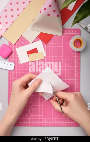 Making a gnome in love craft. Hands cut out a beard from white paper. Creative process. Stock Photo