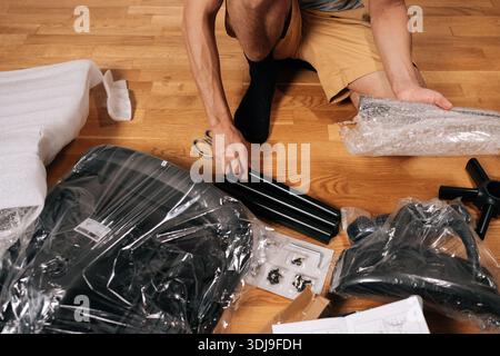 Top view of contractor male unboxing and assembling new flat-pack office chair for home office, carefully unpackaging components on hardwood floor Stock Photo