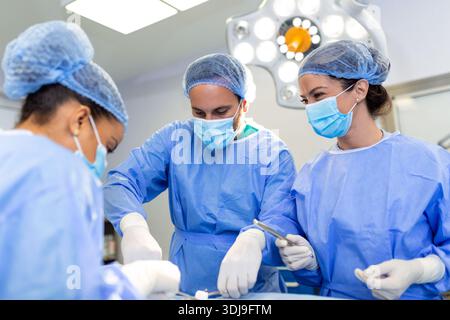 Team of doctors are standing in emergency room. Multi-ethnic surgeons are working at operating room at hospital. They are wearing blue scrubs. Stock Photo