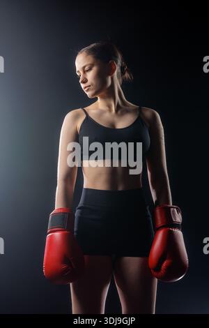 Athletic woman in boxing gloves stands in dramatic studio lighting with copy space, ideal for website banners, gym ads, and social media promotion. Stock Photo