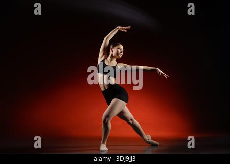 Full length female dancer doing side stretch pose in studio with red Stock Photo