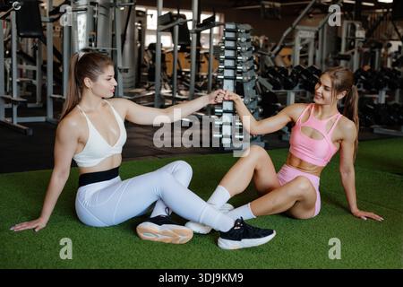 Two fit women friends sitting and relaxing after workout at gym showing support teamwork motivation and healthy lifestyle Stock Photo