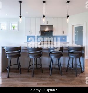 Bright modern kitchen with white cabinetry, island seating, blue tile backsplash and pendant lighting in a clean open concept home interior. Stock Photo