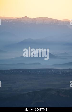 Valley surrounded by Caucasus mountains hills covered in fog and church on top of hill at sunset. Stock Photo