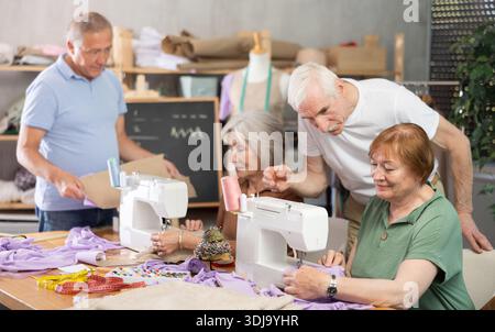 Some people communicate and discuss pattern, while others sew using sewing machine at lesson Stock Photo