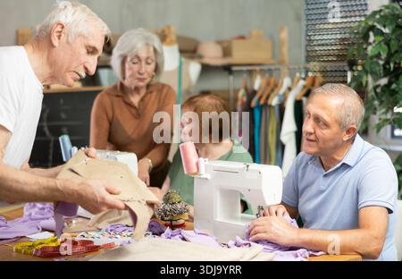 Some people communicate and discuss pattern, while others sew using sewing machine at lesson Stock Photo