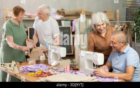 Some people communicate and discuss pattern, while others sew using sewing machine at lesson Stock Photo