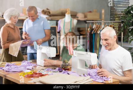 Some people communicate and discuss pattern, while others sew using sewing machine at lesson Stock Photo