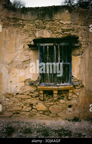 An aged and weathered wall featuring a rustic wooden window with metal bars, capturing the charm of historical architecture Stock Photo