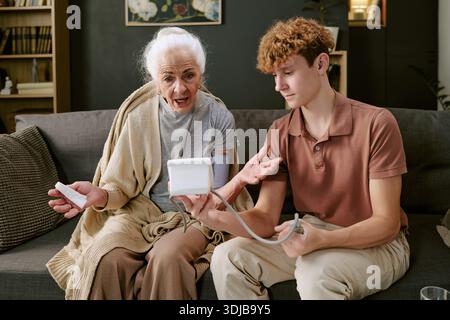 Senior Caucasian Woman Talking While Young Caucasian Man Measuring Blood Pressure Stock Photo