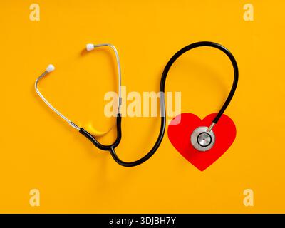 Black stethoscope is checking red heart shape on yellow background, representing healthcare and cardiology Stock Photo