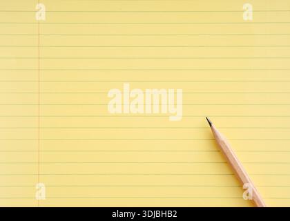 Close-up view of a sharpened pencil resting on a vibrant yellow legal pad, poised for writing notes or capturing ideas Stock Photo