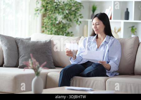 Asian woman checking letter sitting on a sofa at home Stock Photo